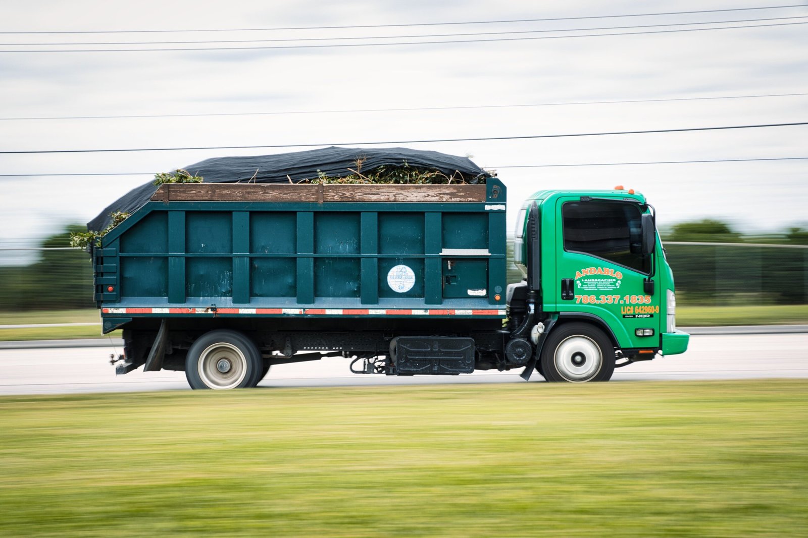 A green truck transporting yard waste on a road captured in motion. Perfect for transportation and environmental themes.